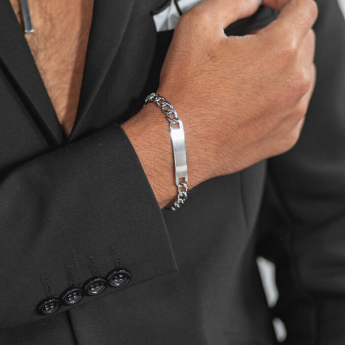 צמיד קובני לגבר "אורגון" צבע כסף עם לוחית לחריטה על יד ימין של דוגמן בז'קט שחור ללא חולצה. זום אין רק על היד