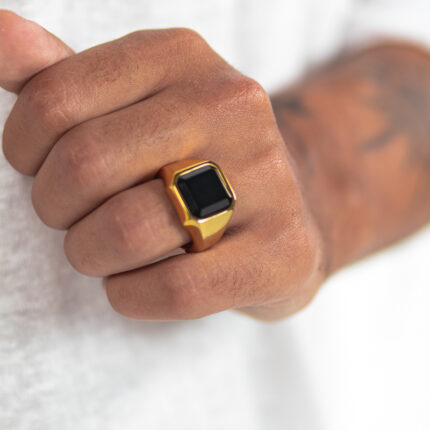 טבעת לגבר "קרנסטון" בצבע זהב מסטיינלס סטיל ואבן שחורה בצורת ריבוע על הקמיצה של דוגמן זום רק על היד מוצמדת לבטן